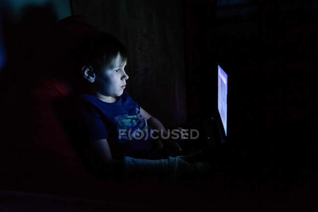 Niño sentado y usando un ordenador portátil, mirando a la pantalla de la computadora - foto de stock
