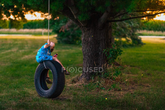 Хлопчик у піжамі на гойдалках у шинах з спалахом світла, що збирає вогняні мухи — стокове фото