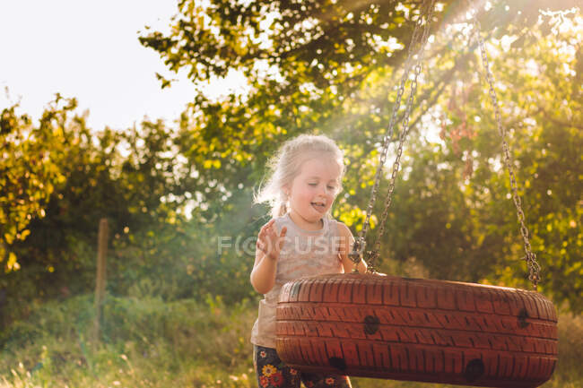 Щаслива маленька дівчинка влітку грає з гойдалкою з колеса — стокове фото