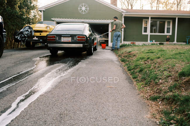 Joven lavando un coche clásico en su entrada en la noche de primavera - foto de stock