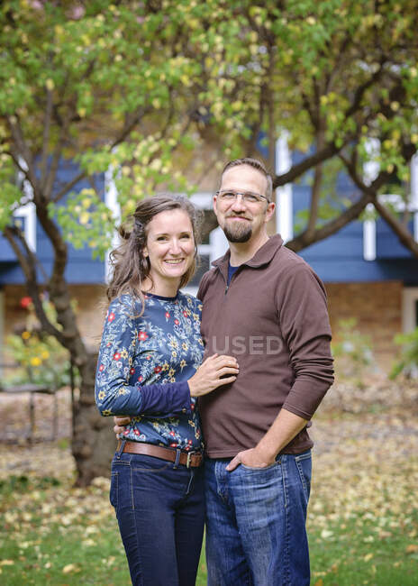 Casal feliz em pé na frente da casa azul e árvores. — Fotografia de Stock