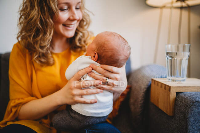 Белая блондинка-мать улыбается своему новорожденному ребенку дома — стоковое фото