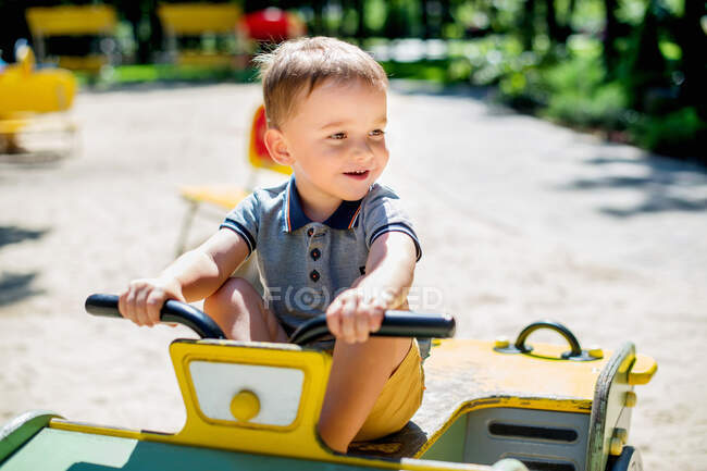 Чарівна 2-річна дитина їде на дерев'яному авто на дитячому майданчику літнього парку — стокове фото