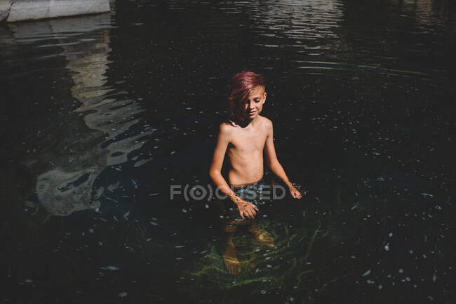 Улыбающийся подросток с розовыми волосами стоит в вихре темной воды — стоковое фото