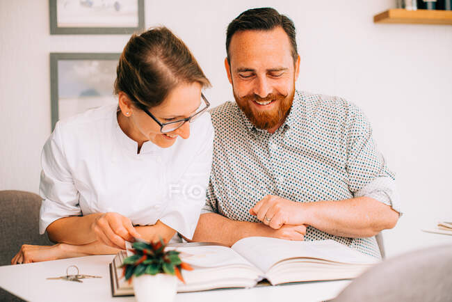 Пара счастливо улыбается, глядя на альбом — стоковое фото