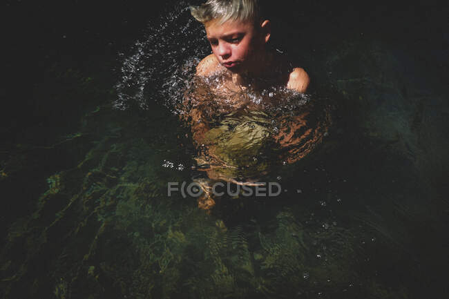 Boy sfonda la superficie dell'acqua con grande pietra — Foto stock