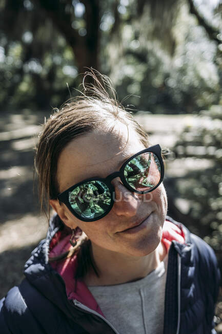 Retrato de una mujer caucásica sonriente con gafas de sol de espejo verde. - foto de stock