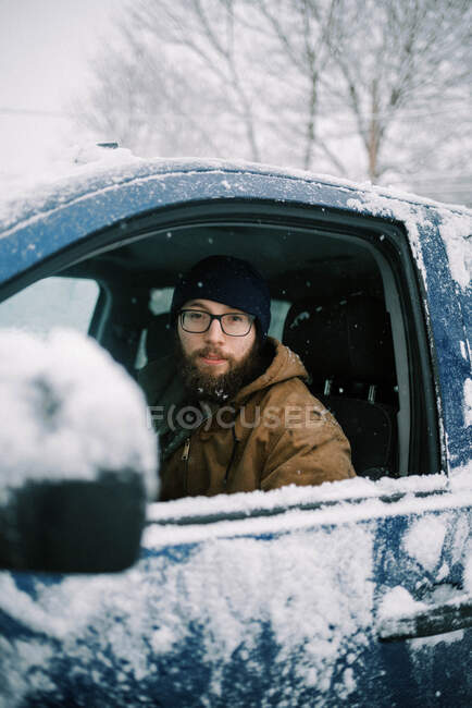 Hombre en camión en la nieve mirando a través de la ventana con gafas y barba - foto de stock