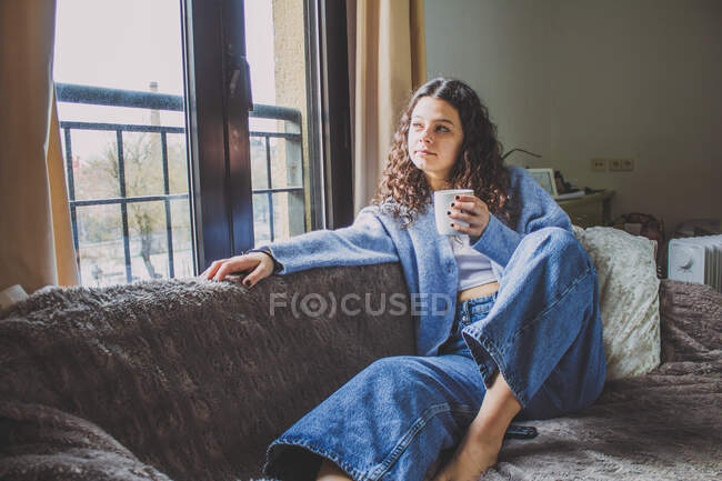 Jeune femme prenant le petit déjeuner sur le canapé avec un café — Photo de stock