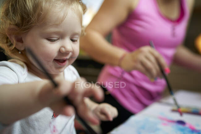 Счастливая улыбающаяся маленькая девочка рисует кисточкой — стоковое фото