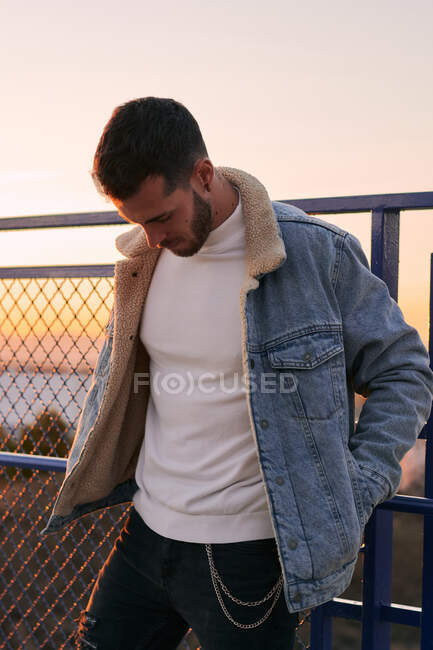 Красивий чоловік в куртці позує на мосту на заході сонця — стокове фото