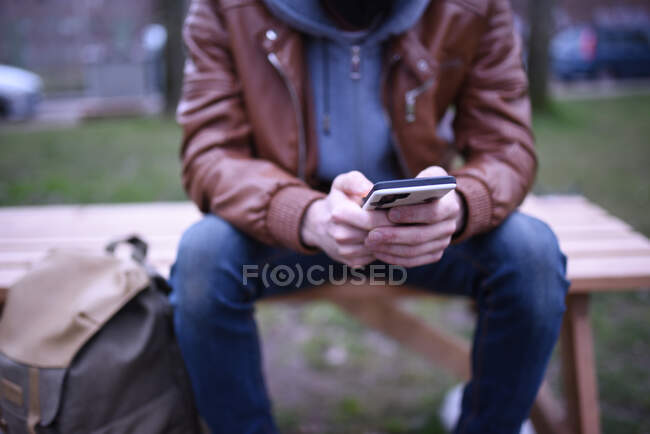 Imagem focada nas mãos de um homem com seu celular em um banco de madeira em um parque. — Fotografia de Stock