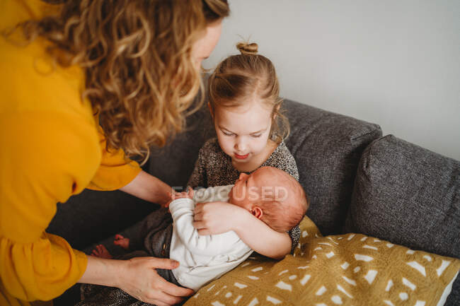 Mutter hilft älterer Tochter, Neugeborenes zu Hause auf Sofa zu halten — Stockfoto