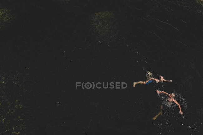 Blick aus der Vogelperspektive auf Zwillingsjungen, die im dunklen Wasser schwimmen — Stockfoto