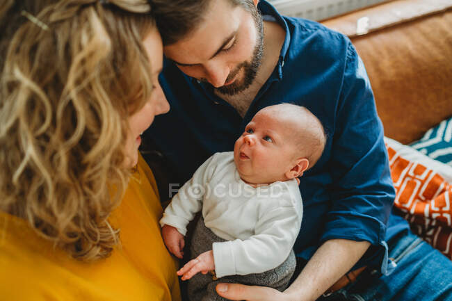 Новорожденный ребенок улыбается своим родителям, сидящим дома на диване — стоковое фото