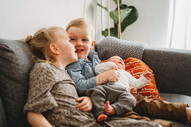 Adorable frère et sœur tenant bébé sur le canapé à la maison pendant la cohabitation — Photo de stock