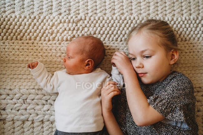 Adorable white sister holding newborn baby's hand at home showing love — Stock Photo