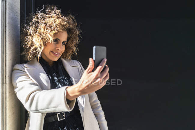 Schöne Frau mit Smartphone an einer schwarzen Wand — Stockfoto