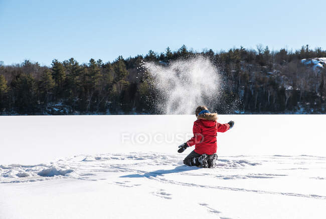 Junge wirft mitten in einem zugefrorenen See Schnee in die Luft. — Stockfoto