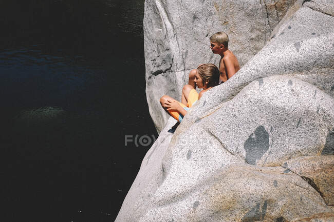 Due ragazzi si siedono al sole estivo sopra l'acqua scura qui sotto — Foto stock