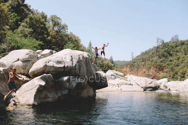 Три мальчика прыгают одновременно в Калифорнийскую плавательную дыру. — стоковое фото