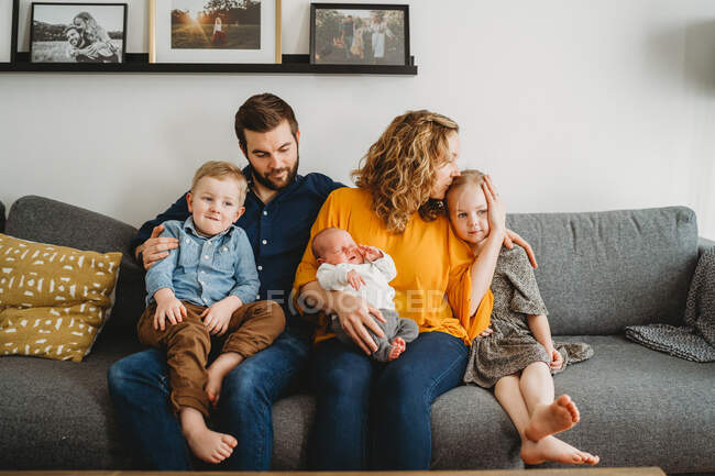 Good looking loving white family holding newborn baby on couch at home — Stock Photo