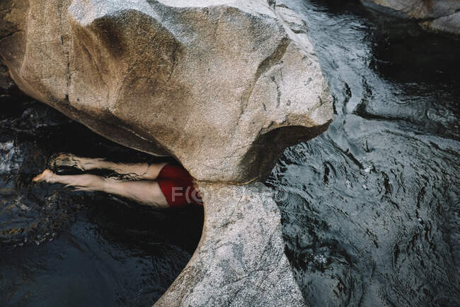 Женщина в красном плавает через каменный проход — стоковое фото