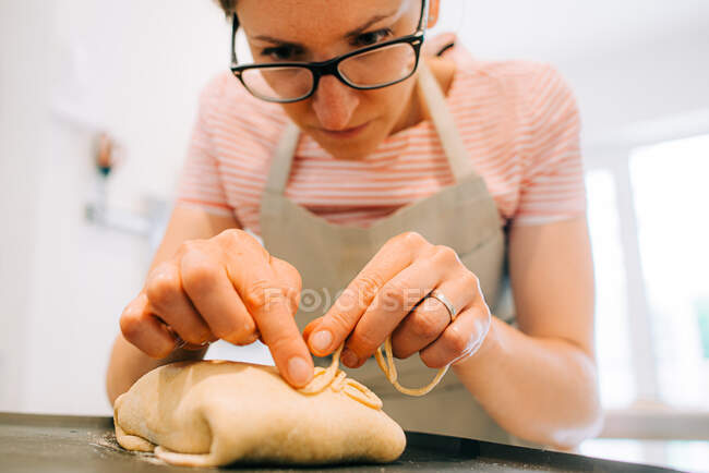 Woman in eyeglasses decorating bread before baking — Stock Photo