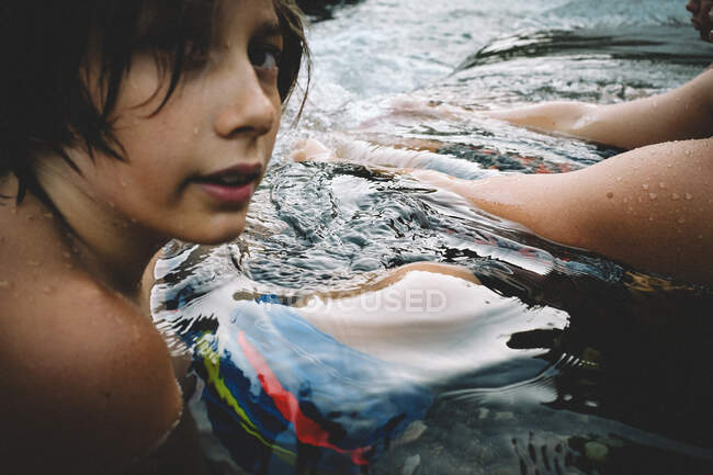 Мальчик-подросток расслабляется в луже воды на закате — стоковое фото