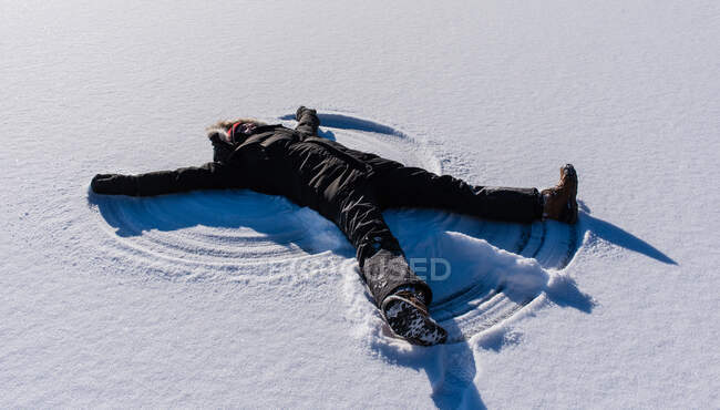 Adulte faisant un ange de neige sur le sol enneigé un jour d'hiver. — Photo de stock