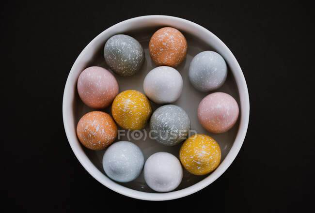 Цветные пасхальные яйца в белой миске на черном фоне — стоковое фото