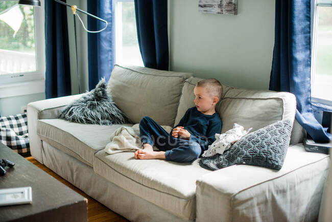 Мальчик отдыхает на диване, смотрит телевизор в одних спортивных штанах. — стоковое фото