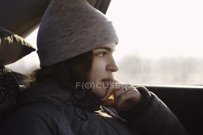 Une fille en vêtements gris regarde par la fenêtre de la voiture, se penche sur sa main. — Photo de stock