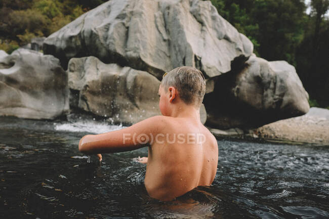 Niño con la piel húmeda se encuentra en la piscina oscura con agua girando a su alrededor - foto de stock