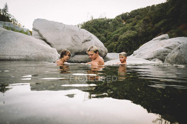Tres chicos se relajan en una piscina de agua al anochecer - foto de stock