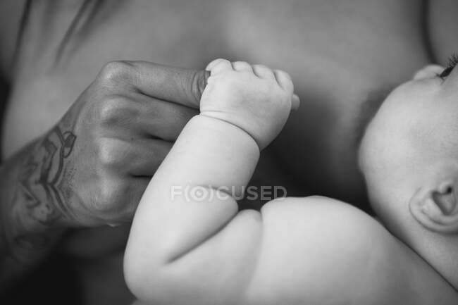 A newborn feeding by breast holding the finger of her young mother — Stock Photo