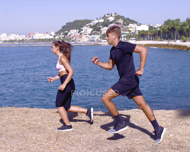 Athletes boy and girl practicing running on the seashore in thei — Stock Photo