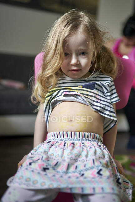 Cute little girl artist sitting on chair showing her pained belly. — Stock Photo