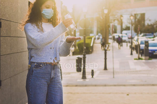 Jeune femme appliquant un gel désinfectant sur ses mains dans la rue — Photo de stock