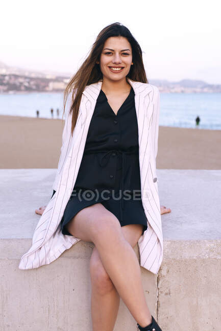 Retrato de uma menina sorridente sentada no cais ao lado da praia — Fotografia de Stock