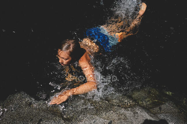 Boy in Bright Trunks Swims and Splashes in a Dark Pool — Stock Photo
