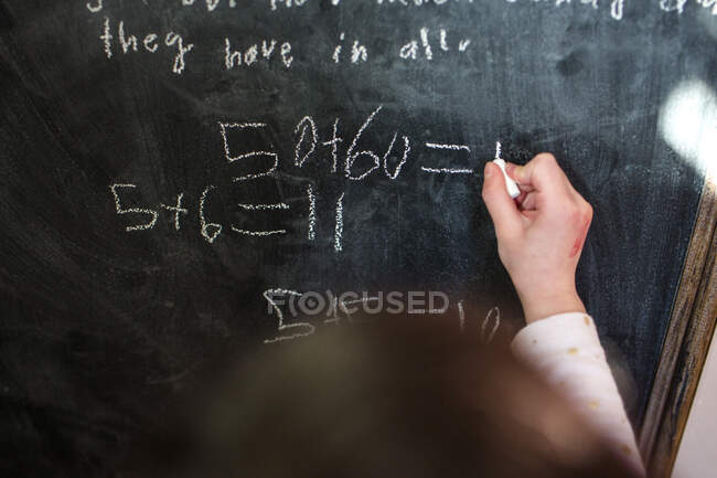Close-up of a small child writing mathematical equations on chalkboard — Stock Photo