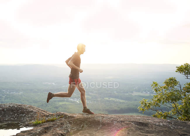 Corredor de trilha masculino adulto em um cume de montanha ao pôr do sol — Fotografia de Stock