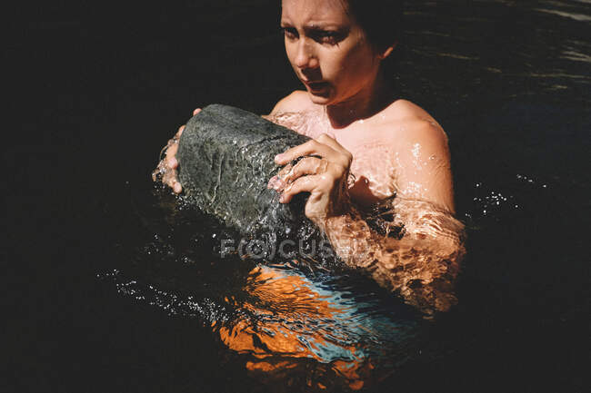 Мальчик прорывается через поверхность воды большим камнем — стоковое фото