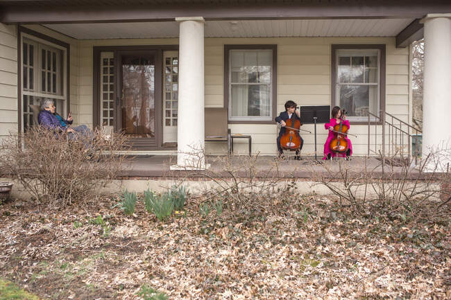 Vue lointaine de deux enfants donnant concert de violoncelle pour femme âgée — Photo de stock