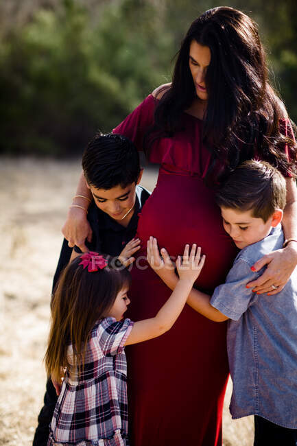 Bambini che abbracciano la madre incinta in campo a San Diego — Foto stock