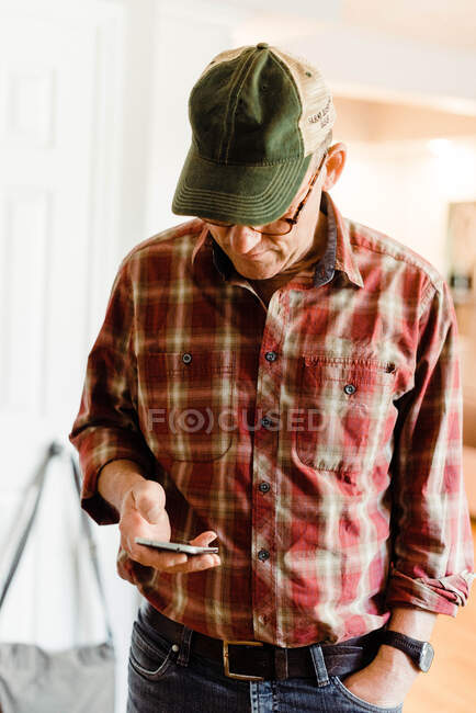 Mann mittleren Alters steht im Zimmer, während er sein Smartphone liest — Stockfoto