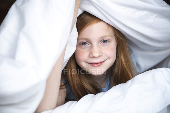 Bella ragazza in camicia bianca si trova su un divano in camera da letto con un cuscino. — Foto stock