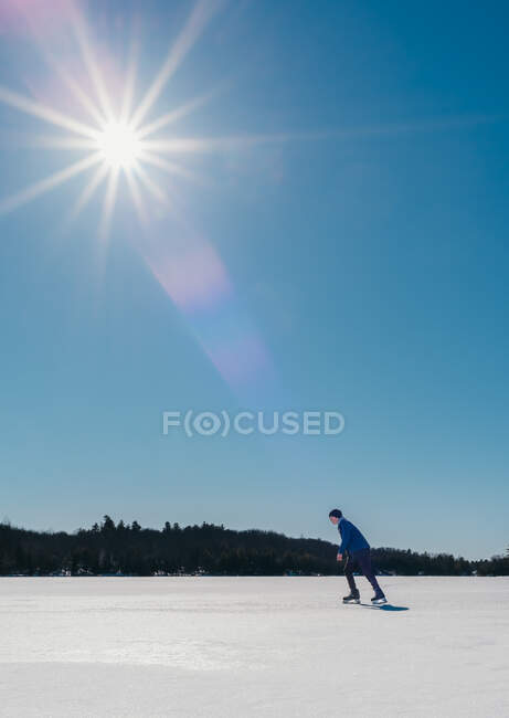 Мальчик-подросток катается на коньках по замерзшему озеру в Канаде в солнечный зимний день. — стоковое фото