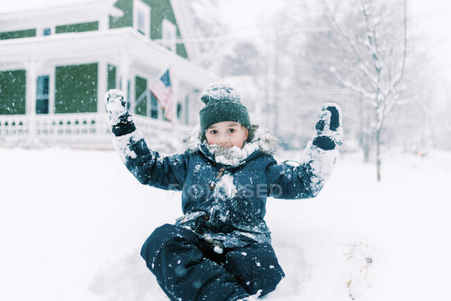 Маленький мальчик, сидящий в сугробе перед своим домом во дворе — стоковое фото